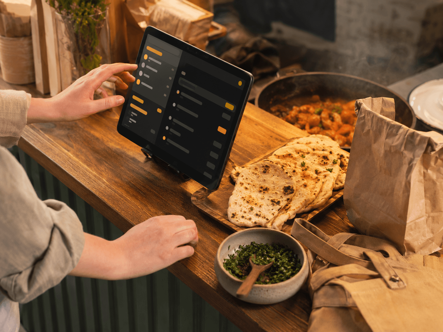 Helfer am Holz-Tresen bedient Tablet mit Echtzeit-Bestellübersicht